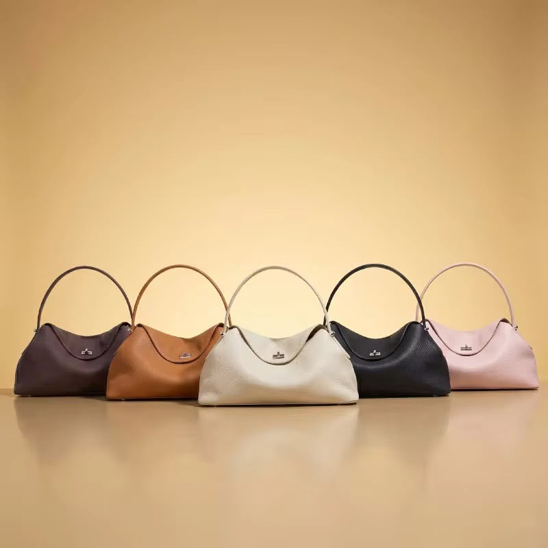 Five slouchy crescent-shaped leather shoulder bags in dark purple, tan, off-white, black, and light pink, lined up on a warm beige reflective surface.
